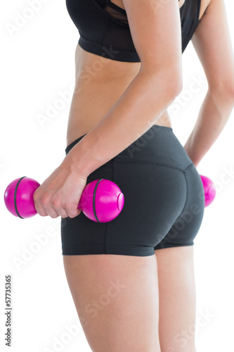 Mid section of sporty young woman holding pink dumbbells