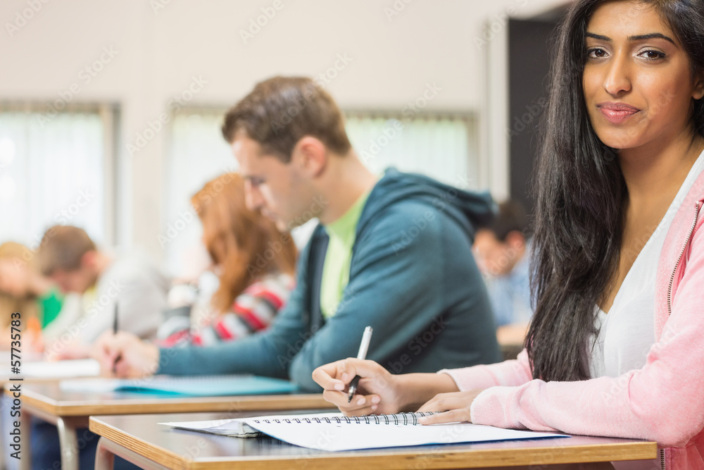 Female student with others writing notes in classroom Female student with others writing notes in classroom