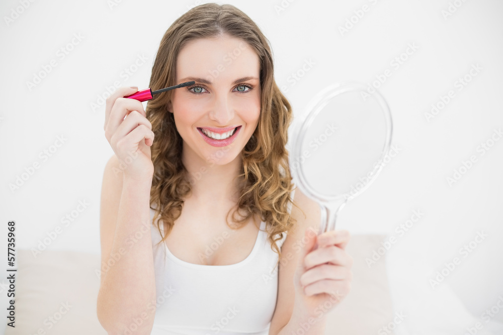 Young woman using mascara while holding a mirror Young woman using mascara while holding a mirror