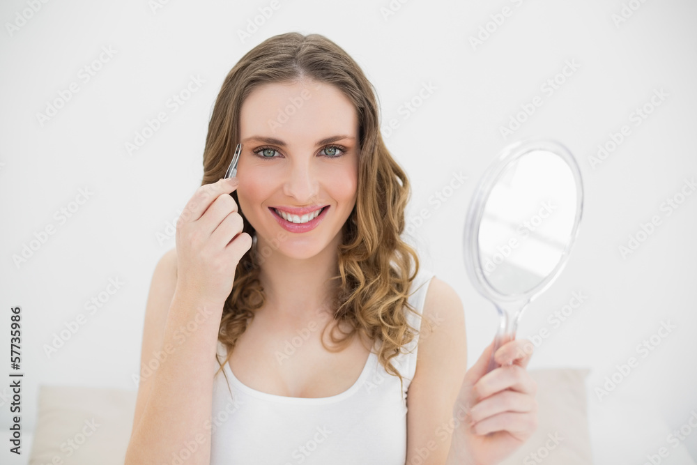 Pretty woman plucking her eyebrows while smiling into the camera Pretty woman plucking her eyebrows while smiling into the camera