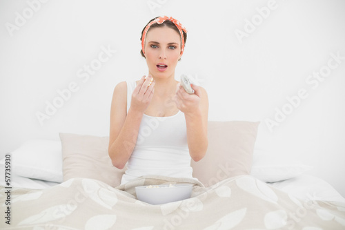 Surprised woman watching television eating popcorn
