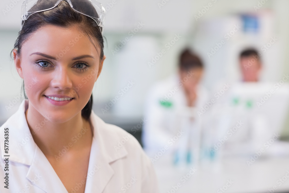 Female researcher with colleagues in background at lab Female researcher with colleagues in background at lab