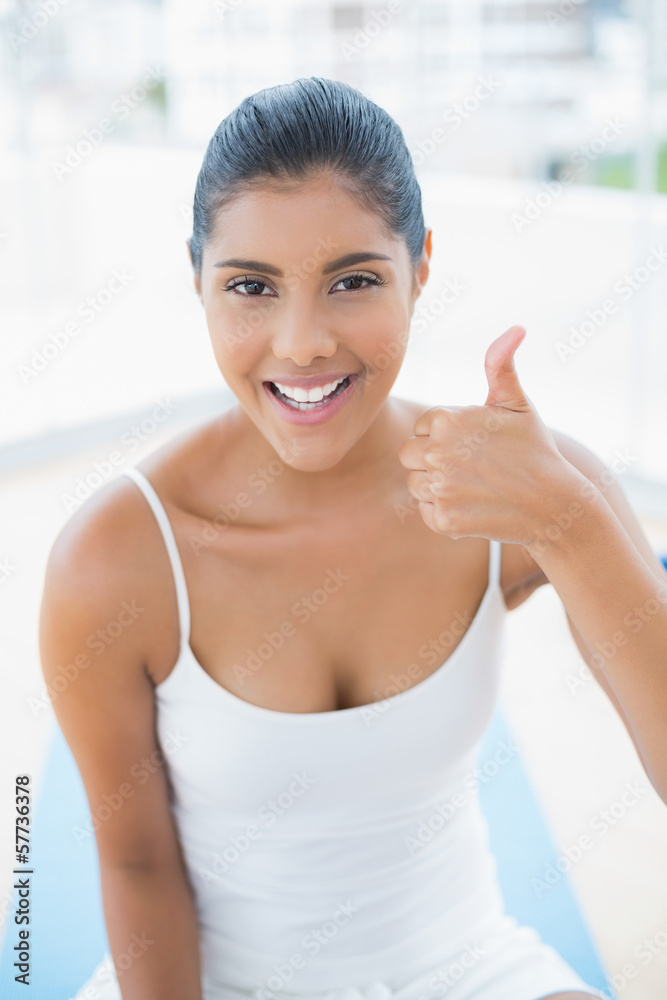 Smiling toned brunette sitting on floor showing thumb up