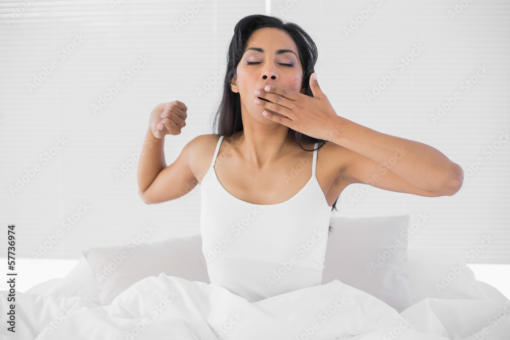 Cute young woman yawning while sitting on her bed Cute young woman yawning while sitting on her bed
