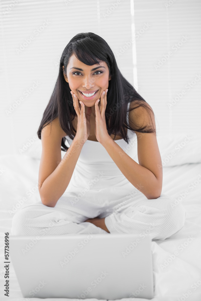 Lovely smiling woman sitting on bed in front of her notebook Lovely smiling woman sitting on bed in front of her notebook