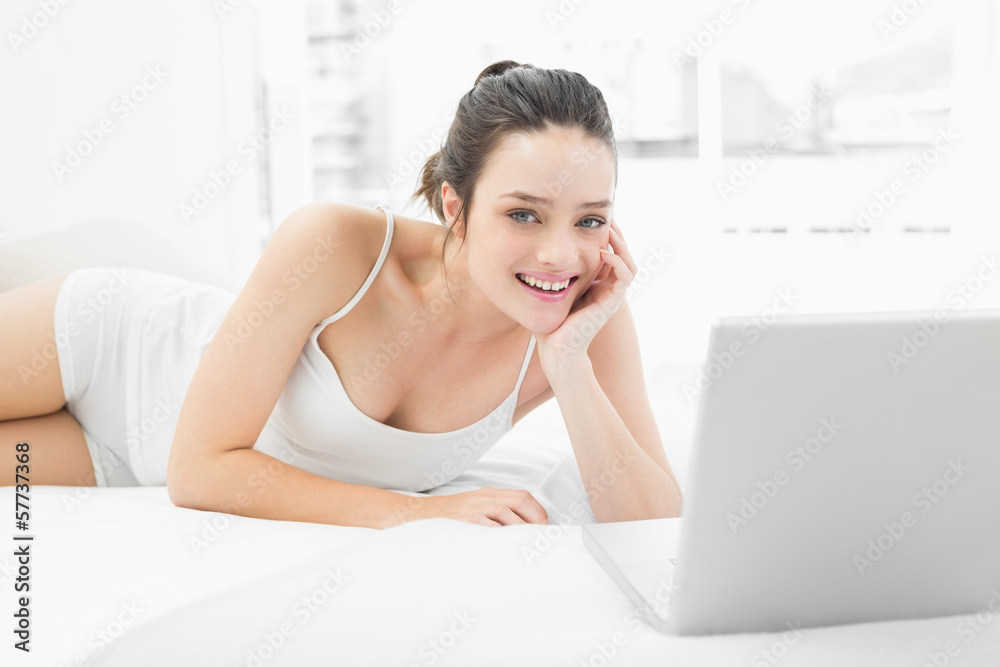 Smiling casual woman with laptop lying in bed Smiling casual woman with laptop lying in bed