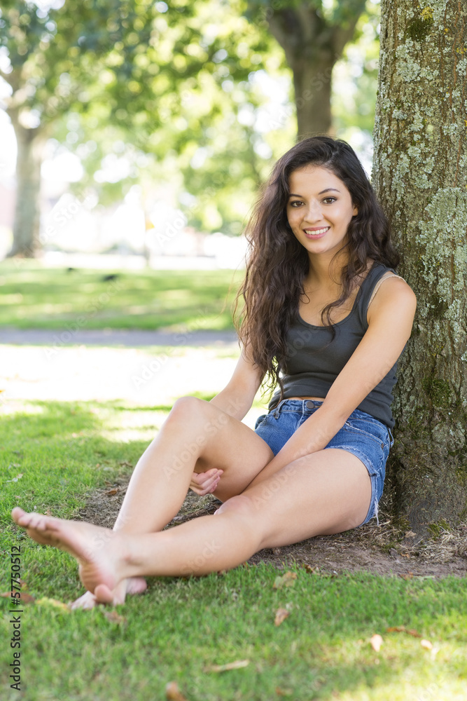 Casual smiling brunette sitting leaning against tree Casual smiling brunette sitting leaning against tree