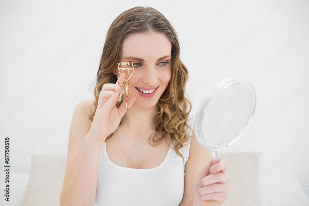 Woman using an eyelash curler while looking into a mirror Woman using an eyelash curler while looking into a mirror
