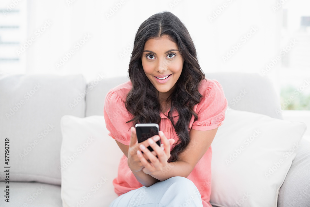 Happy cute brunette sitting on couch holding smartphone Happy cute brunette sitting on couch holding smartphone