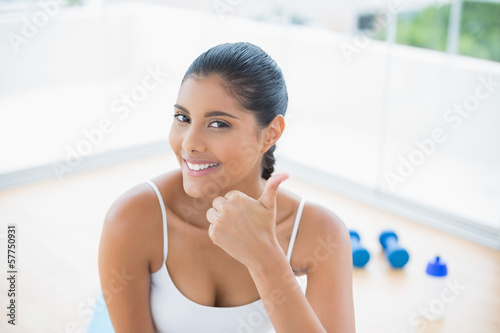 Free Download Happy toned brunette sitting on floor showing thumb up - GFXLoad