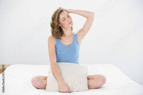 Attractive woman posing sitting on her bed holding a pillow