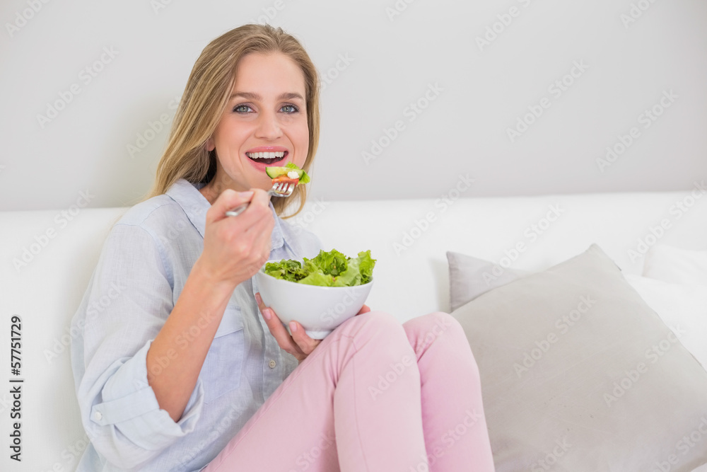 Smiling casual blonde sitting on couch eating salad Smiling casual blonde sitting on couch eating salad