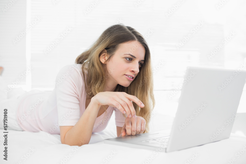Lovely brunette woman using her notebook lying on her bed Lovely brunette woman using her notebook lying on her bed