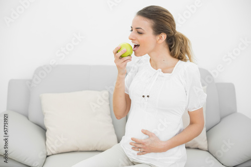 Lovely pregnant woman eating green apple while touching her bell