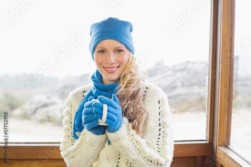 Woman with cup in warm clothing against window