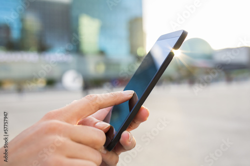 Businesswoman sending messages with her mobile phone, building