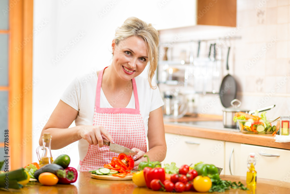 Cute woman cuts paprika for salad sitting at the kitchen table Cute woman cuts paprika for salad sitting at the kitchen table