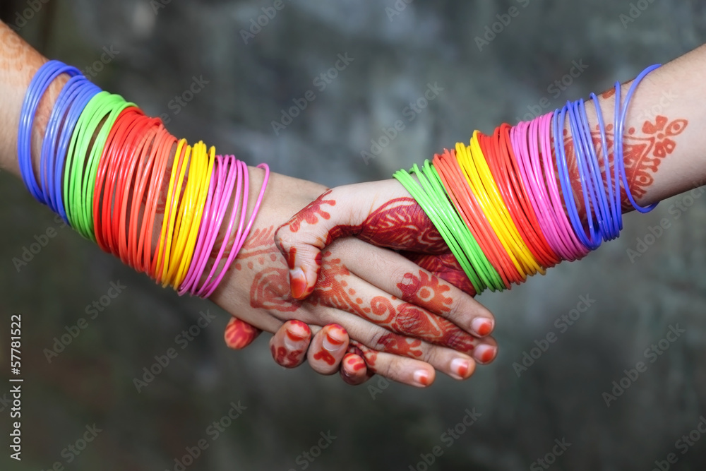 Shaking hands decorated with colorful bracelets and henna tattoo