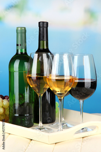 Wine bottles and glasses of wine on tray  on bright background