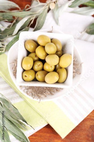 Olives in bowl with branch on napkin on wooden board on table