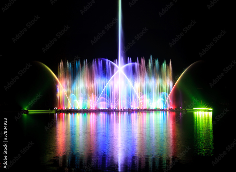 The dancing fountain show has a reflection on the water surface. The background is black.