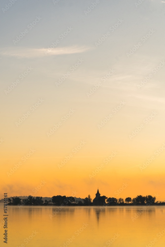 Vertical minimalist view of sunrise over lake with old church.