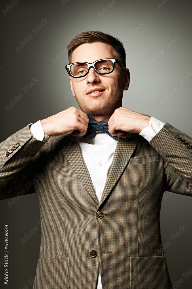 Confident nerd in eyeglasses adjusting his bow-tie Confident nerd in eyeglasses adjusting his bow-tie
