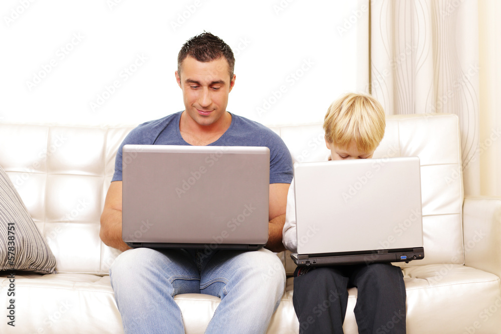 Father and son working on their computers on the sofa at home Father and son working on their computers on the sofa at home