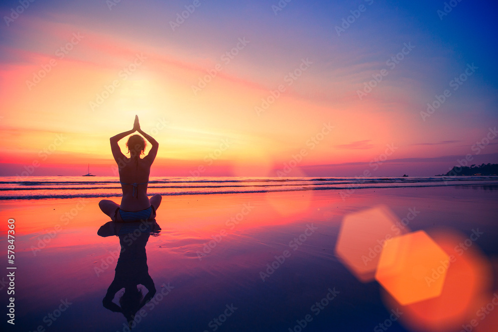 Silhouette yoga woman sitting on sea coast at beautiful sunset.