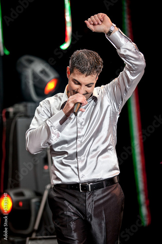 Handsome singer lifting up left hand while singing on stage photo