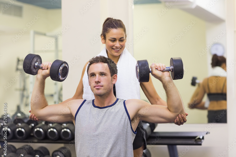Trainer correcting muscular man lifting dumbbells Trainer correcting muscular man lifting dumbbells