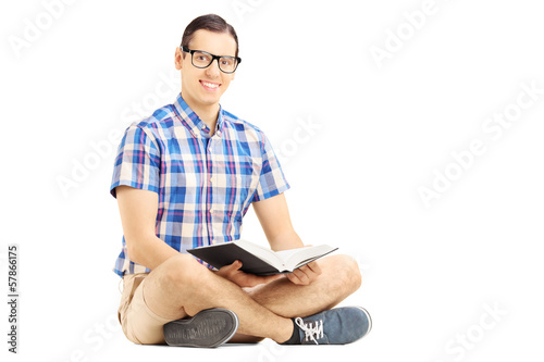 Smiling guy with glasses sitting on a floor and reading a book