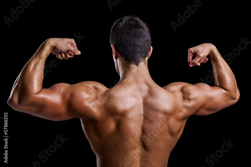 Muscle young man showing his back muscles against a dark backgro