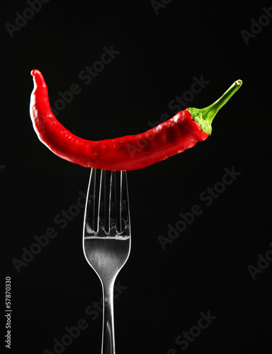 Red hot chili pepper on fork, isolated on black
