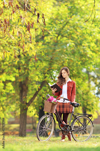 Young woman with bicycle in a park reading book
