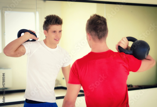 Two young men in gym working out with kettlebells