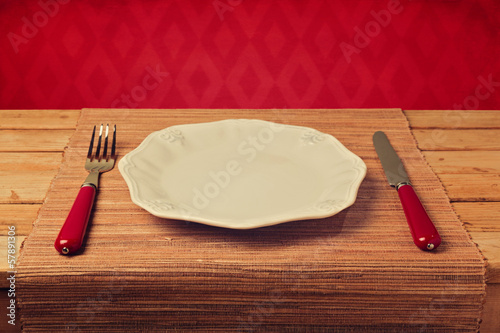 Empty plate with knofe and fork on placemat over wallpaper photo