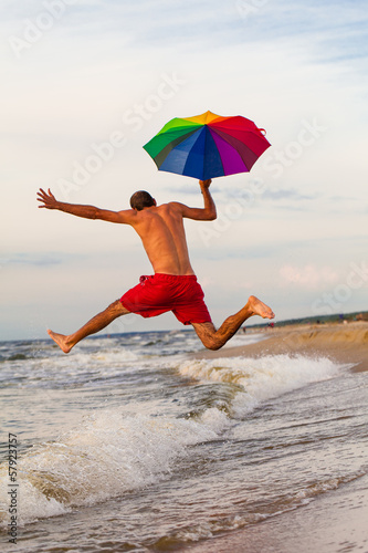 Fototapeta Naklejka Na Ścianę i Meble -  Happy man jumping with umbrella on the beach
