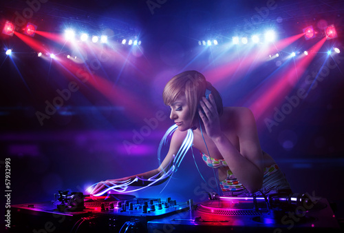 Disc jockey girl playing music with light beam effects on stage