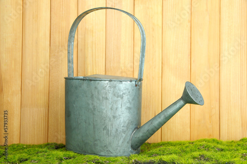 Watering can on grass on wooden background