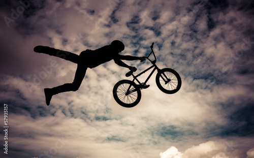 Silhouette of a man doing an jump with a bmx bike.