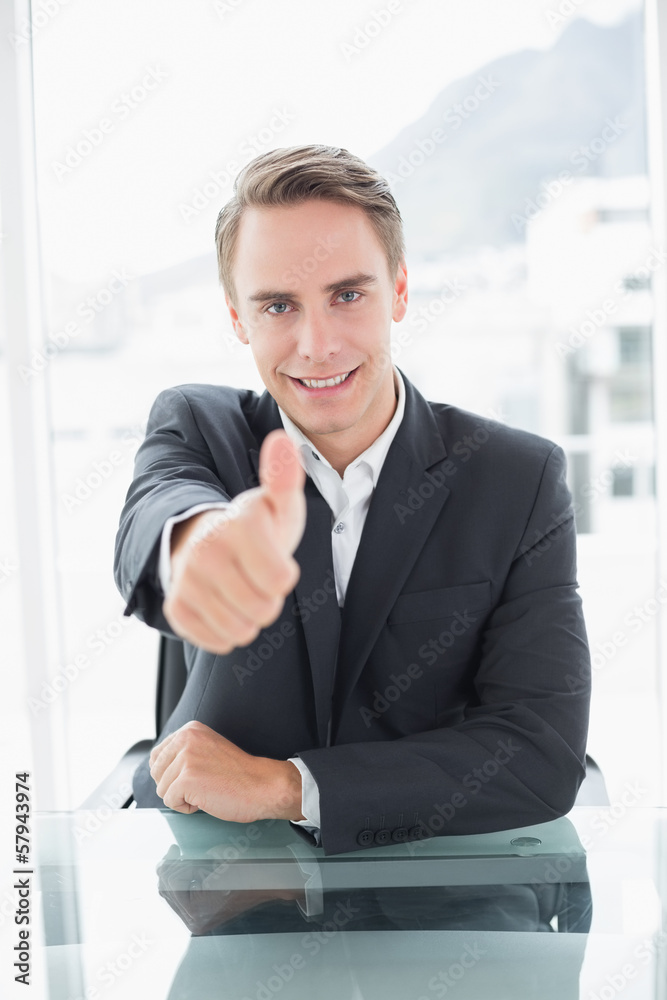Smiling businessman gesturing thumbs up at office desk Smiling businessman gesturing thumbs up at office desk