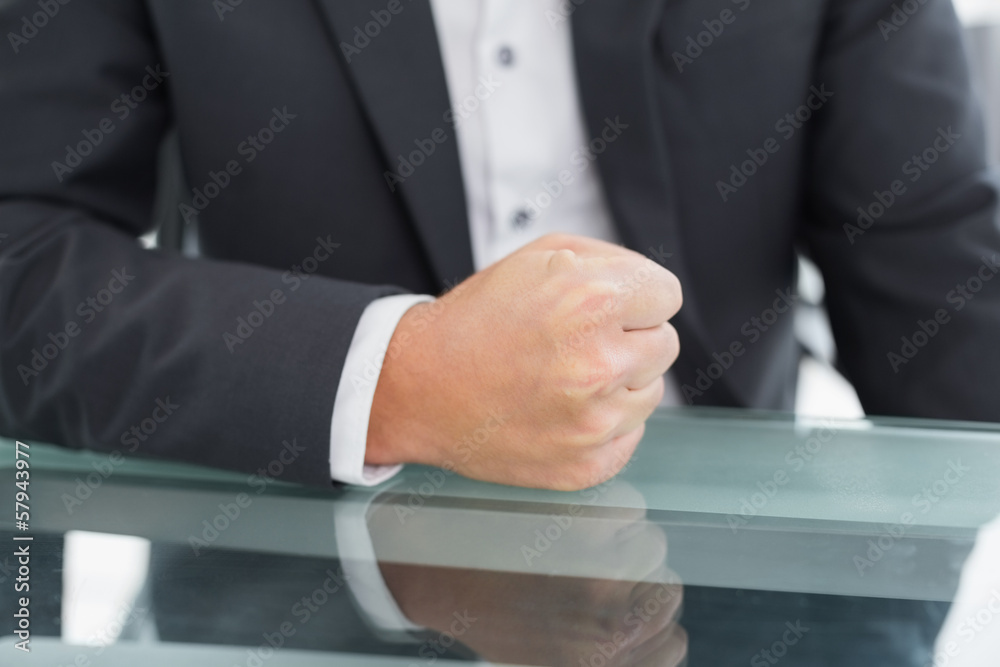 Mid section of businessman with clenched fist on office desk