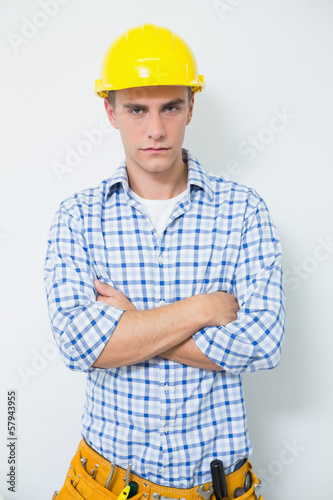 Serious handyman in yellow hard hat with arms crossed