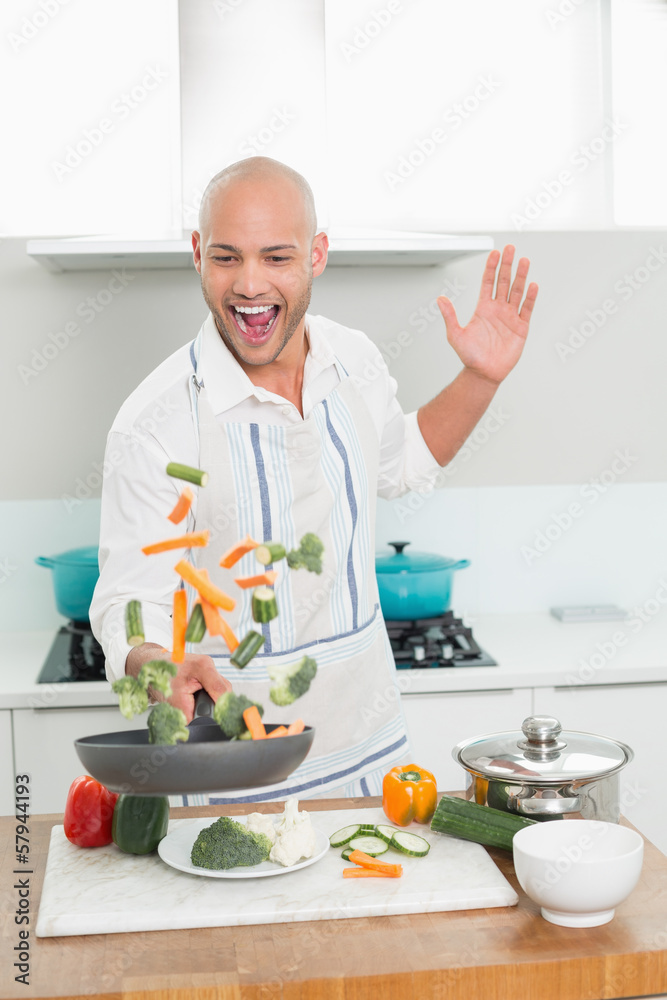 Cheerful man tossing vegetables in kitchen