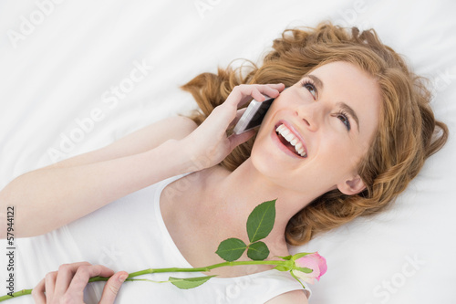 Woman using mobile phone while resting in bed with rose