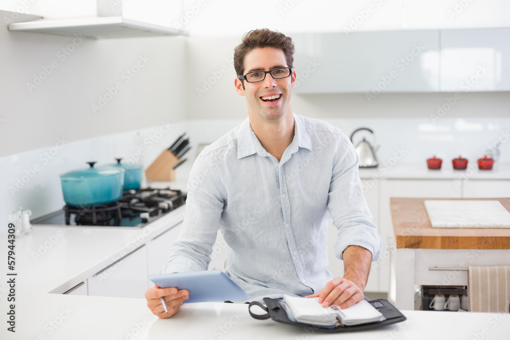 Cheerful casual man with digital tablet and diary in kitchen