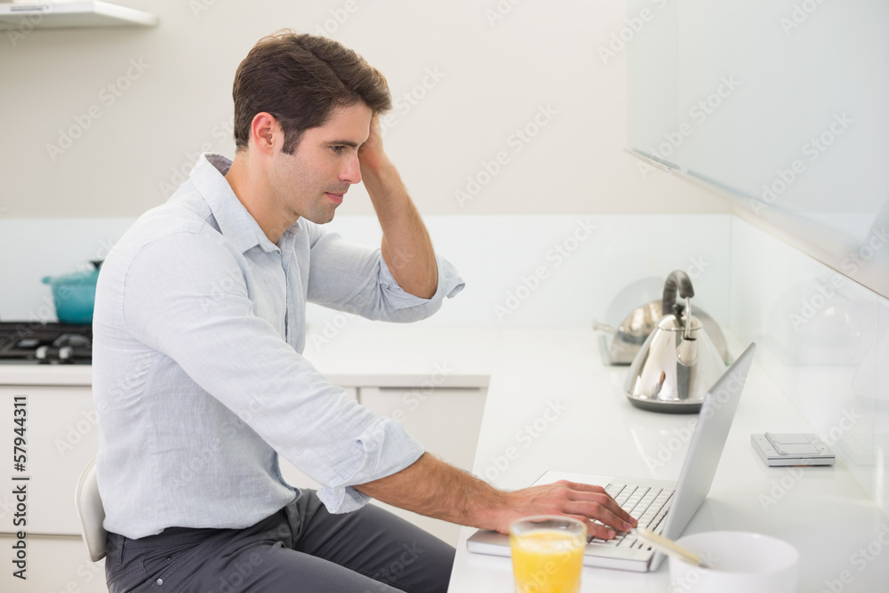 Concentrated casual man using laptop in kitchen