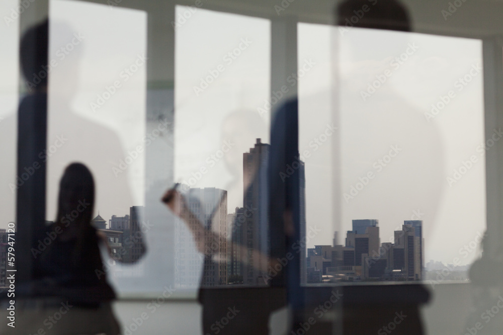 Three business people standing and looking at a white board on the other side of a glass wall Three business people standing and looking at a white board on the other side of a glass wall