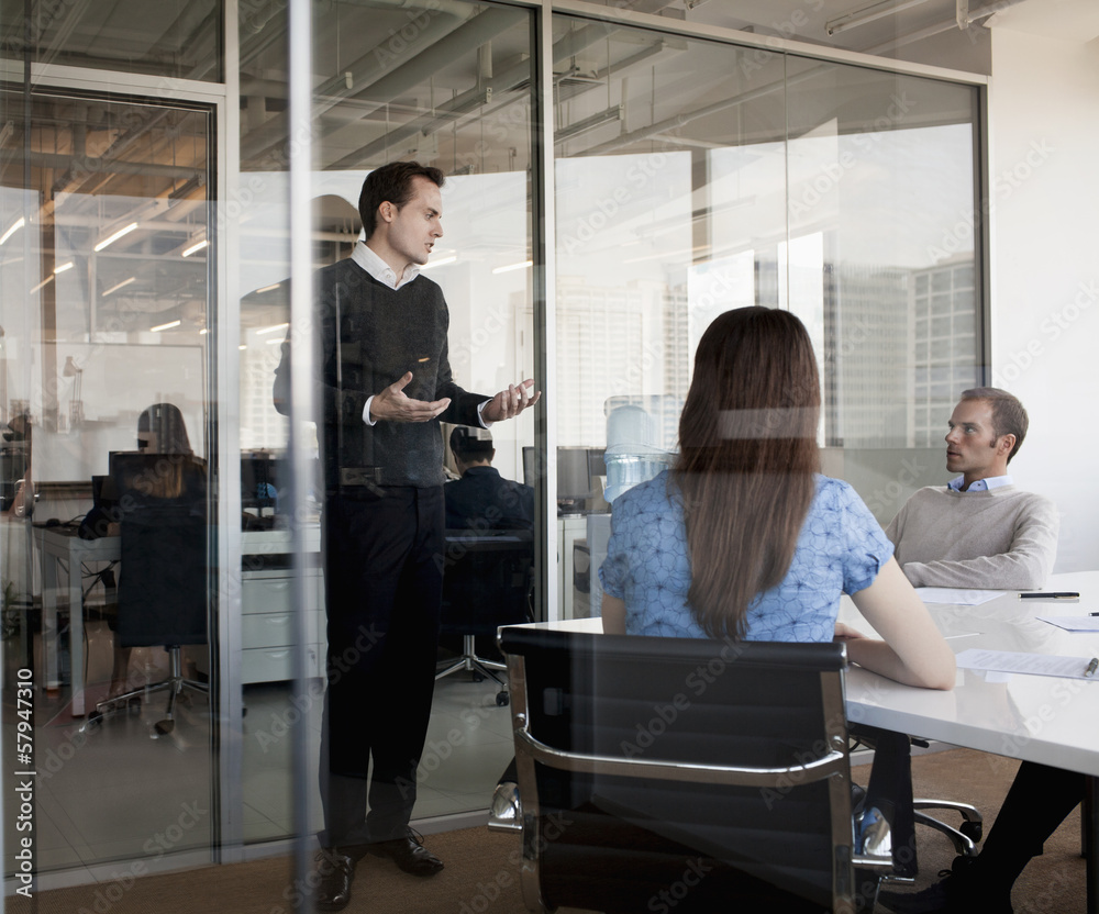 Three business people sitting, standing, and discussing during a business meeting Three business people sitting, standing, and discussing during a business meeting